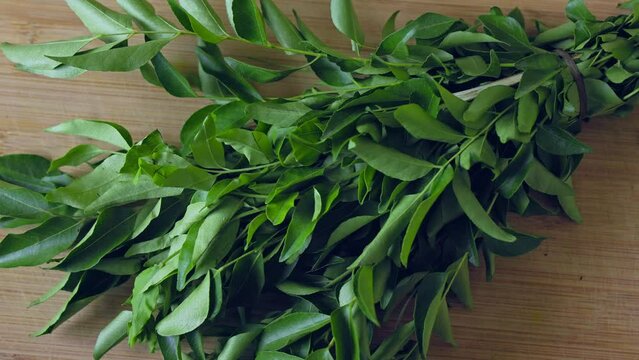 A closeup of a bunch of fresh, lush curry leaves on a wooden chop board