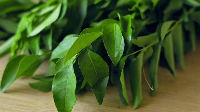 A closeup of a bunch of fresh, lush curry leaves on a wooden chop board