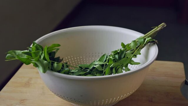 A male hand gently placing a bunch of fresh, lush curry leaves in plastic basket