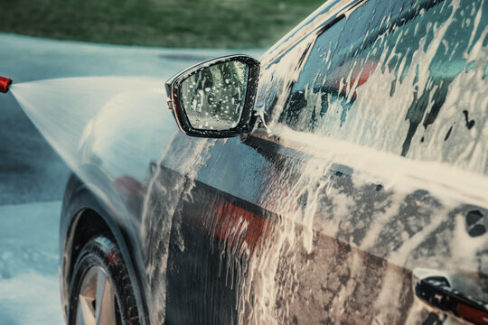 A car covered in soapy suds while being washed at an outdoor self-service  car wash station