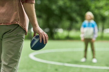 Fototapeta premium Closeup of father and son playing American football together outdoors in park, focus on hand holding ball, copy space