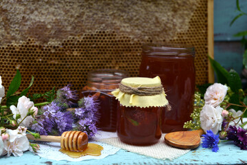 Still life with natural honey in jar, dipper, flowers and stick against background of honeycomb in...