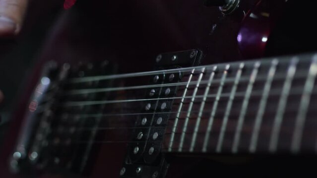 Musician standing on a stage with the concert lighting during the show, start playing electric guitar with a pick and taking first notes close up