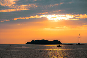 Beautiful sunset over the sea with silhouette of a lighthouse and boats