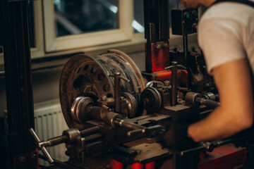 Handsome auto mechanic in red uniform fixing disk for wheel alignment at the car service