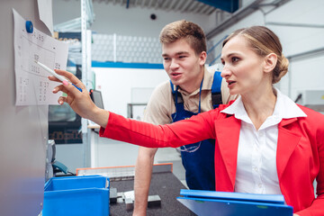 Worker and manager on factory floor discussing product specifications looking at a plan sheet