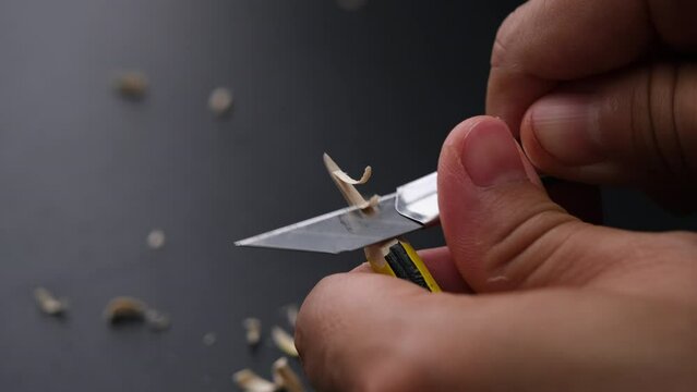 Hands sharpening pencil using utility knife, close up.