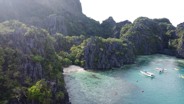 Aerial pullback reveals stunning cove with double outrigger canoes secluded in el nido philippines