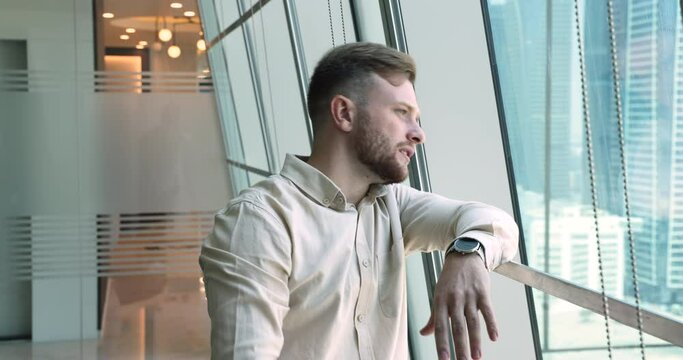 Pensive concerned young man stand alone in company hallway wait for job interview turn feels nervous look out window. Office employee searching for new ideas, thinks of problem solution, ponder indoor