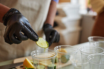 Close up of woman wearing glove adding lime slices to refreshing lemonade drinks in bar, copy space