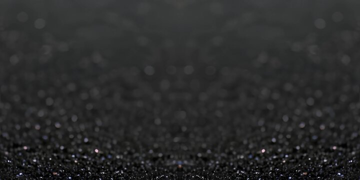 Black sand glittering texture defocus surface closeup. Empty distance background.