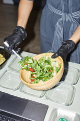 Closeup of female hands putting salad into plastic containers while working in food delivery or doing meal prep, copy space