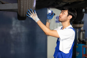 mechanic using flashlight for checking tire and fixing underneath the car