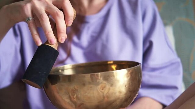 A woman with red hair is sitting at home on the bed and doing meditation with a singing bowl. 