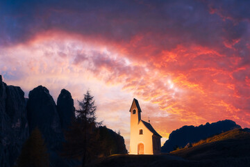 Incredible view on small iIlluminated chapel - Kapelle Ciapela on Gardena Pass, Italian Dolomites mountains. Colorful sunset in Dolomite Alps, Italy. Landscape photography - obrazy, fototapety, plakaty