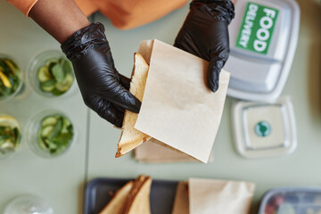 Top view of unrecognizable woman wearing gloves packing turkey sandwich for food delivery, copy...