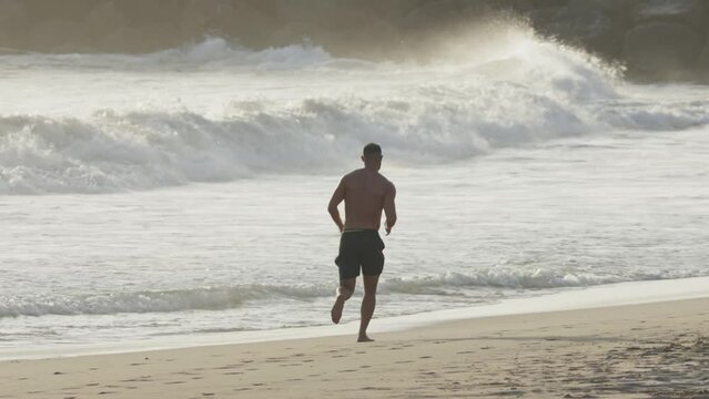 A man jog on beach at sunset in waves