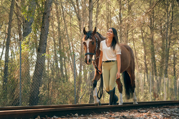 Horsewoman walking with horse along railroad