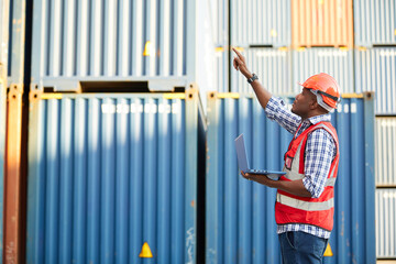 African factory worker or engineer working on laptop computer and pointing pose in containers warehouse storage