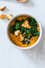 Healthy curry creamy soup with seasonal summer vegetables, sunflower seeds,  croutons, healthy vegan meal in rustic bowl, directly above