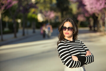 Obraz premium Young and beautiful woman, Hispanic, brown hair, with striped sweater, linen pants and sunglasses, with her arms crossed, angry and arrogant. Concept angry, disgust, arrogance.