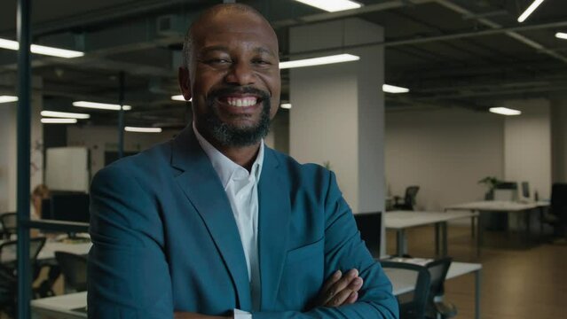 Portrait of happy mature black man in businesswear looking at camera by desk in office