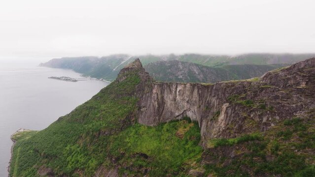 Aerial view close to a mossy, green, mountain wall, revealing the rocky coastline of Lofoten islands, Norway pan, drone shot