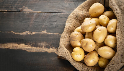 Raw potato food . Fresh potatoes in an old sack on wooden background. Free place for text. - obrazy, fototapety, plakaty