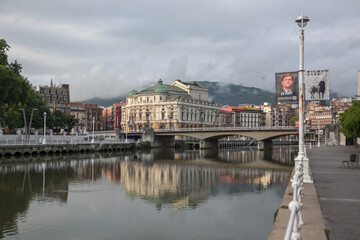 Fototapeta na wymiar Exterior view at the Nervión river and Areatzako zubia bridge, Arriaga square, an iconic plaza on Casco Viejo, Arriaga Theatre, Bilbao downtown city, Spain