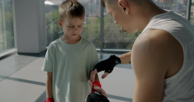Adult man caring father teaching little boy how to wrap hands prepare for fight in sports club. Active lifestyle and fatherhood concept.