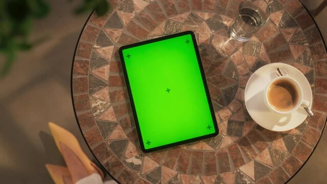 Top Down View of a Tablet Computer with Mock Up Green Screen Display. Static Footage of a Device Lying on a Coffee Table. Woman Reading her Favorite E-Book While Drinking Coffee Outdoors