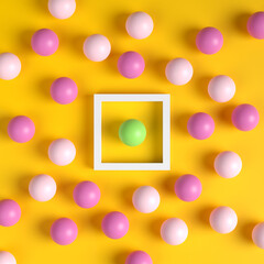 Green ball in a white frame surrounded by pink balls outside the box on yellow background. Difference, individuality, standing out from the crowd.