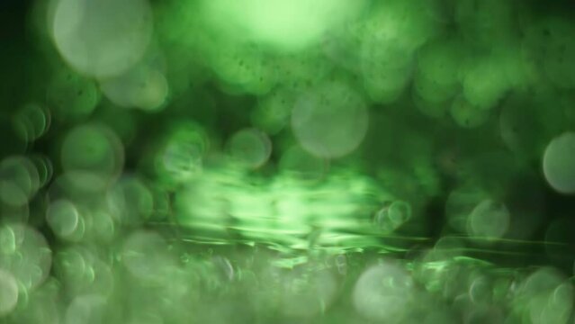 Macro close up super slow motion 1000fps. Splash drops liquid in green color.Shine water drops liquid when surface water is vibration. Wave and drops in green background.Flying flicker vibrant effect