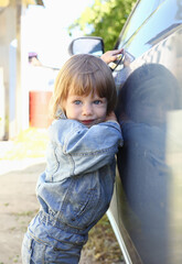 Little fashion child holds the car handle in a jeans jacket smiles and looks into the camera...