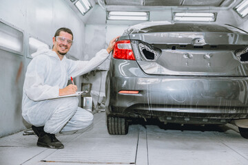 car body painter professional male worker checking color paint detail in auto garage bodywork shop