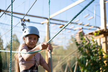 Little Girl Having Fun in a Rope Park Trail Facility. Happy little child enjoying climbing in an...