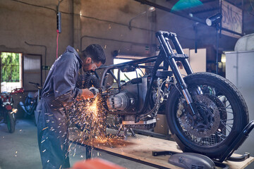 Fototapeta na wymiar Mechanic using angle grinder while repairing motorcycle