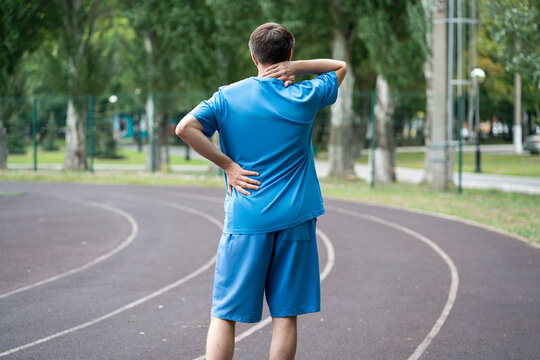 Back pain, athletic man with backache on a running track after workout