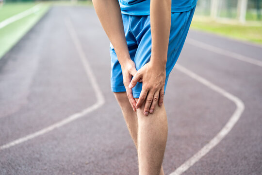 Diseases of the knee joint, bone fracture and inflammation, athletic man on a running track after workout suffering from pain in leg and doing self-massage