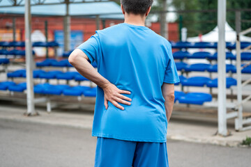 Back pain, kidney inflammation, man suffering from backache on a sports ground after workout