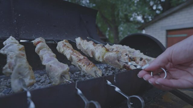 Female flips marinated juicy pork strung on skewers on mangal for barbeque. Marinated meat strung on skewers grills above hot coals for garden party