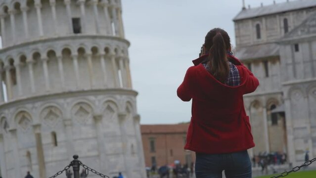 Young female tourist taking photos of the famous Leaning Tower of Pisa, Italy