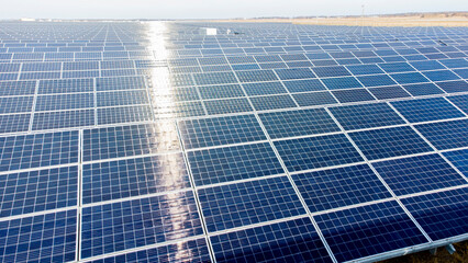 Aerial drone view flight over solar panels on sunny day close-up. Photovoltaic solar panel. Moving over solar panels with sun glare. Production of renewable alternative energy. Green ecological energy