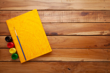 Beautiful Yellow Diary, with some fabric colors, and a paintbrush on the top. Wooden background. Top view.