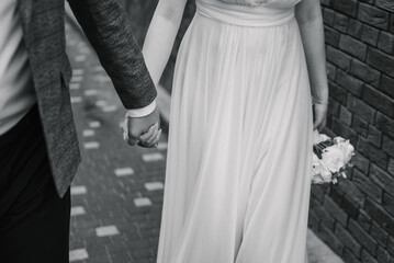 Bride and groom hold hands and walking on the street. Closeup. Details of wedding moments. Newlyweds together. Bride and groom walk outdoors. Bottom down view. Black and white photo. Couple hands.
