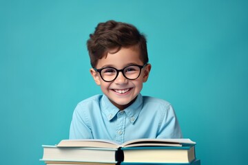 portrait of a happy child little boy with glasses sitting on a stack of books and reading a books, light blue background.