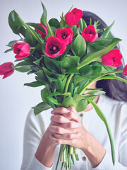 Anonymous woman holding bouquet of red flowers in front of face