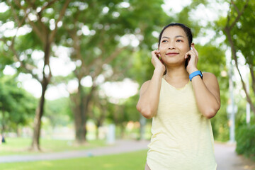 Beautiful smart and good looking Asian adult woman checking on a smartwatch or fitness tracker while practicing running - jogging at the park.