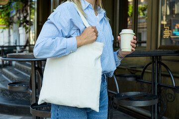 Cotton white bag on female shoulder and paper cup in hand outdoors