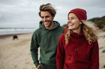 A man and woman wearing red and green hoodies on the beach. AI